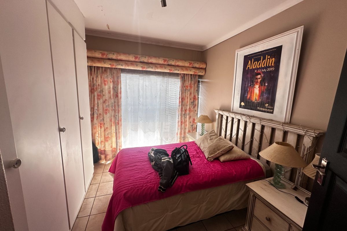 A bedroom featuring tiled flooring, built-in cupboards, and a ceiling-mounted spotlight, with visible ceiling water staining requiring attention.