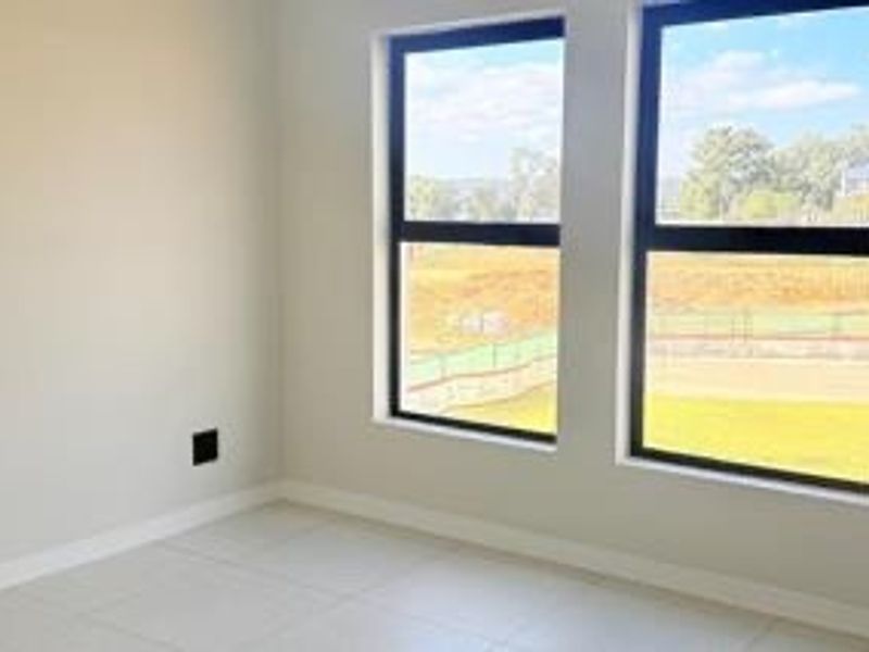 A bright, empty bedroom featuring neutral tiled flooring and large windows that provide ample natural light and a view of the surrounding area.