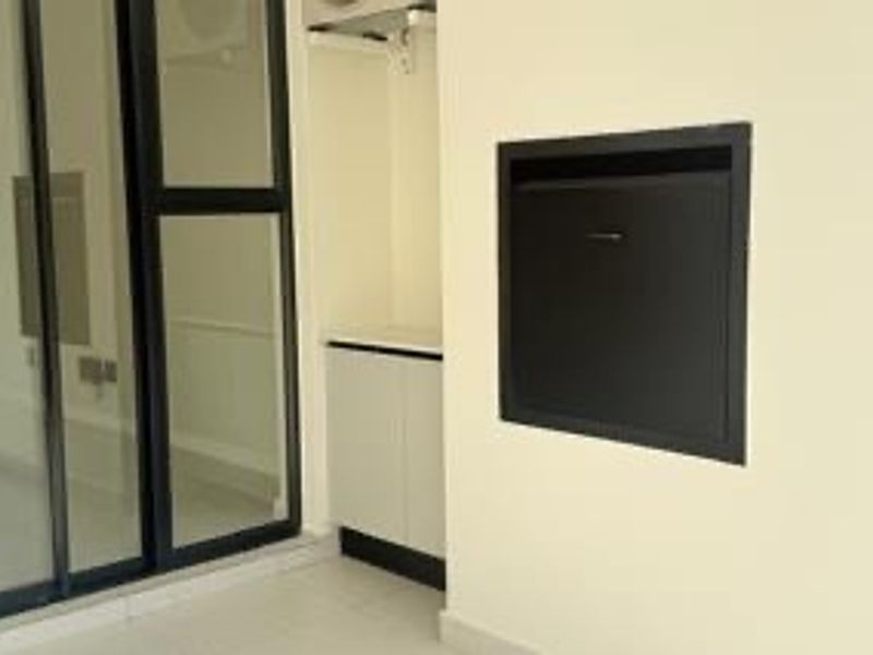 A clean, modern balcony featuring tiled flooring, a sliding glass door, and built-in cabinetry with a wall-mounted utility hatch.