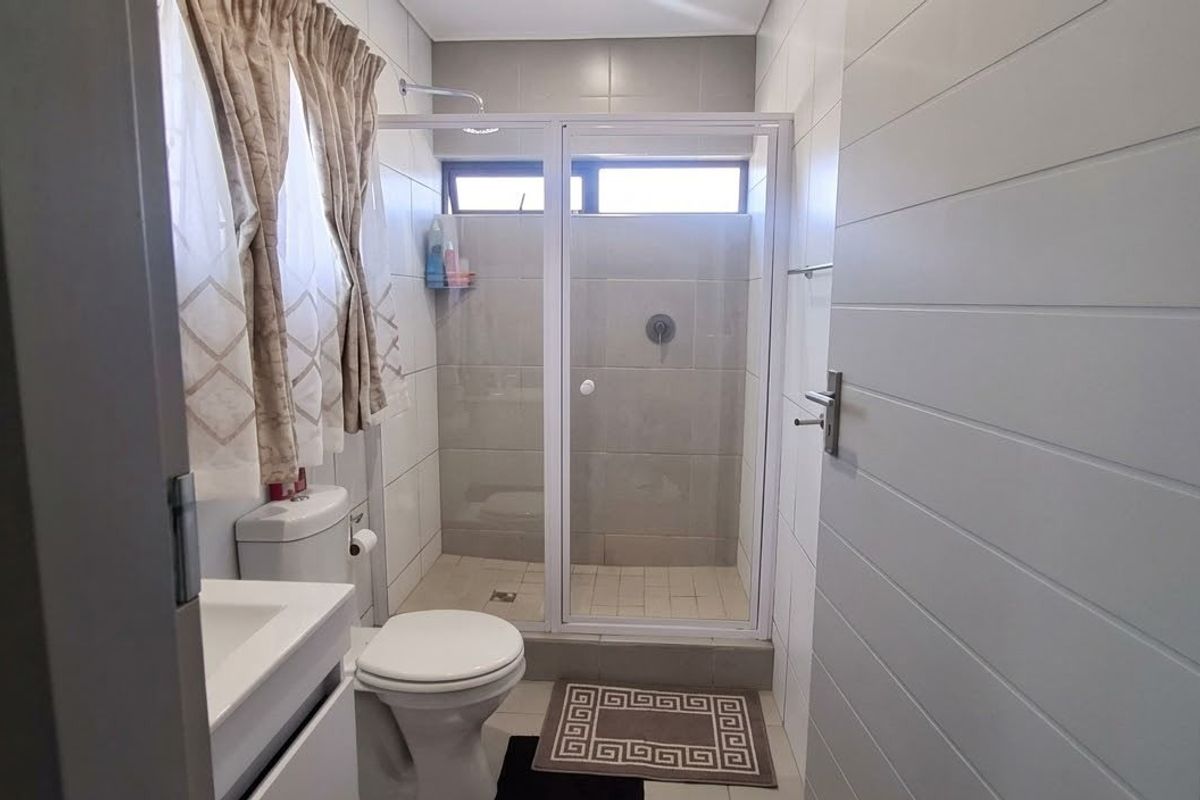 A functional bathroom featuring a glass-enclosed shower, modern vanity basin, and neutral tiled finishes throughout.