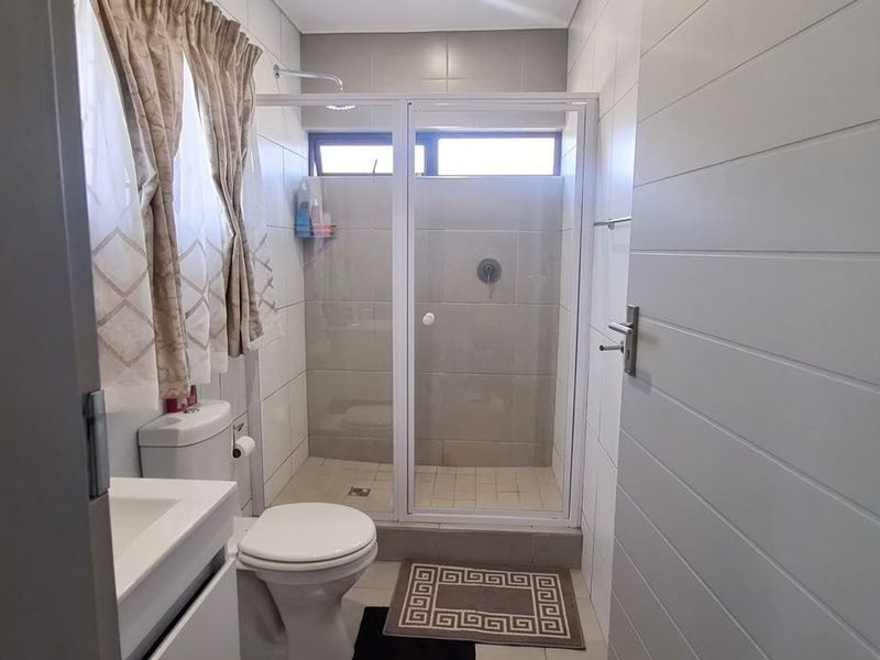 A functional bathroom featuring a glass-enclosed shower, modern vanity basin, and neutral tiled finishes throughout.