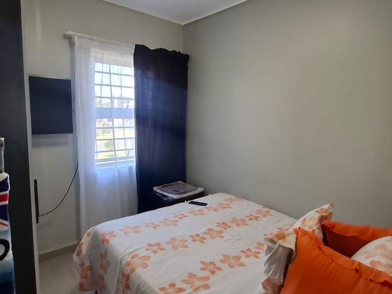 A functional bedroom featuring tiled flooring and a window fitted with security bars, providing natural light and basic security.