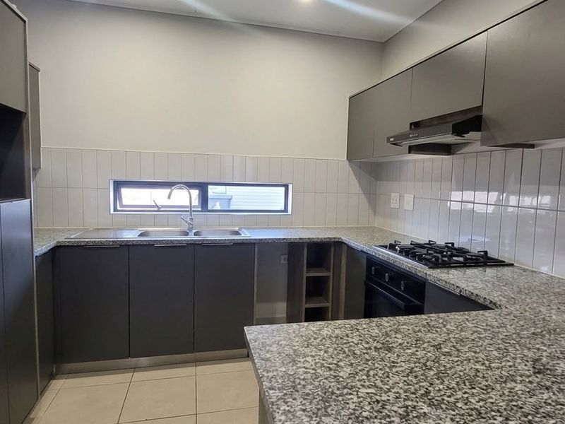 Modern kitchen featuring granite countertops, built-in gas hob, oven, extractor fan, and ample cabinetry with a tiled backsplash.