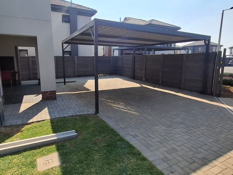 A neat front exterior featuring a paved driveway, a functional metal carport, and secure boundary fencing.