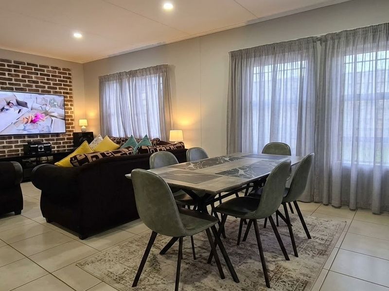 Spacious open-plan living and dining area featuring tiled floors, recessed lighting, and a decorative exposed brick feature wall.
