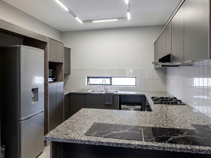 Modern kitchen featuring granite countertops, built-in cabinetry, gas hob, extractor fan, and a tiled backsplash with contemporary recessed lighting.