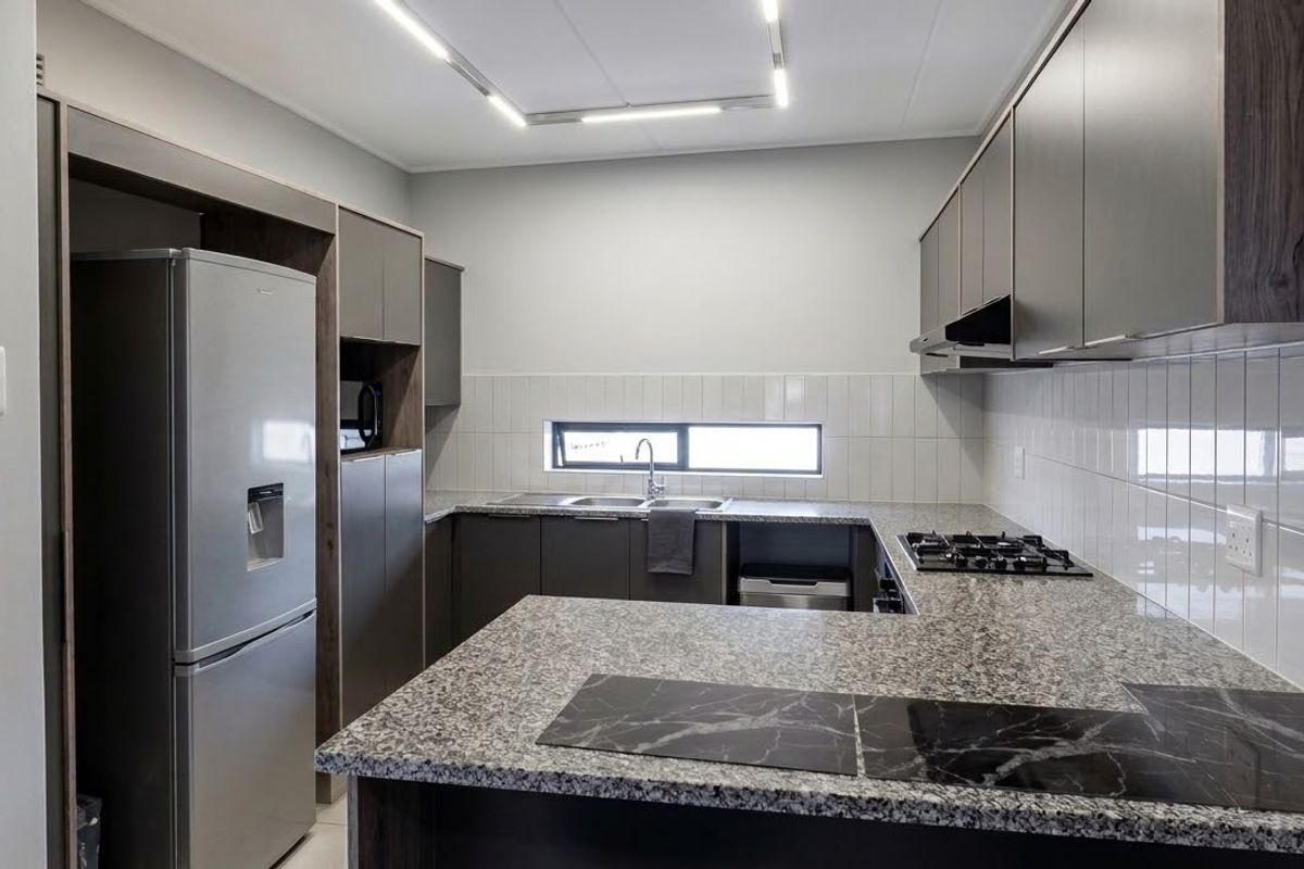 Modern kitchen featuring granite countertops, built-in cabinetry, gas hob, extractor fan, and a tiled backsplash with contemporary recessed lighting.