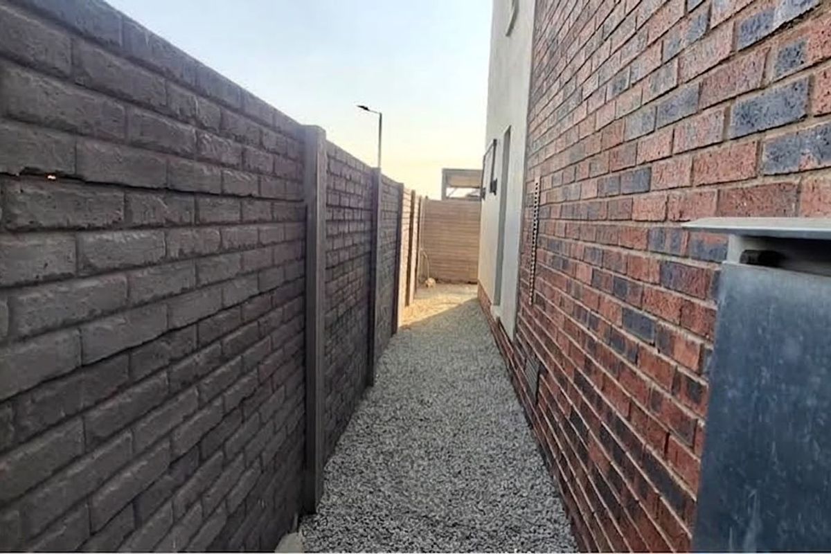 A narrow side passage featuring a gravel pathway bordered by a brick boundary wall and the main house structure.