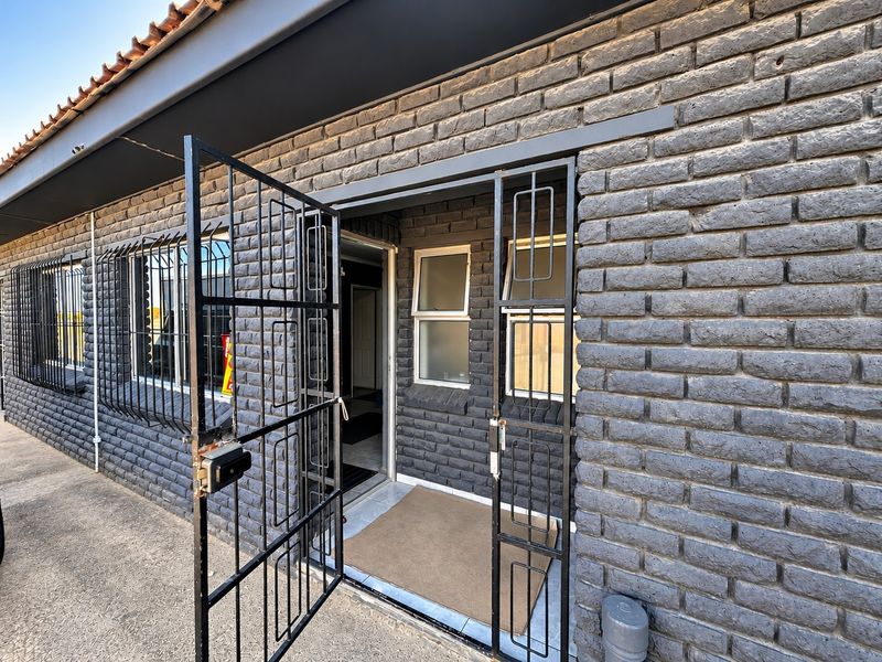 Front entrance of a house featuring dark painted brickwork, security gates, and protective window bars.