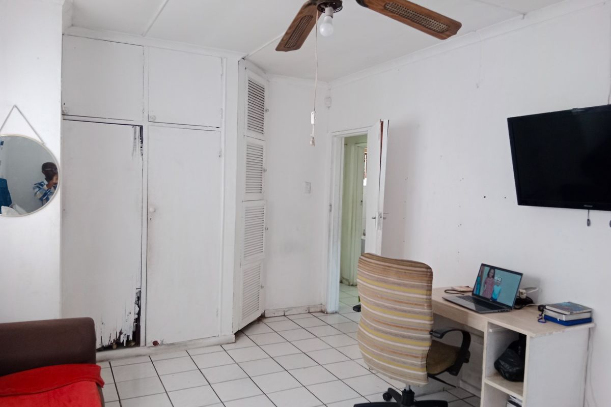 A bedroom featuring tiled flooring, a ceiling fan, and built-in storage cupboards with visible wear on the door finishes.