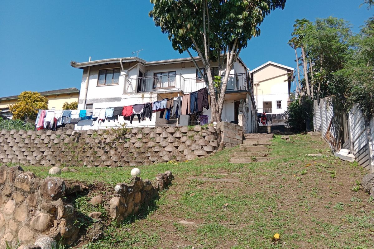 Rear view of a multi-level house featuring a stone retaining wall, concrete stairs, and an upper-level balcony with metal railings.