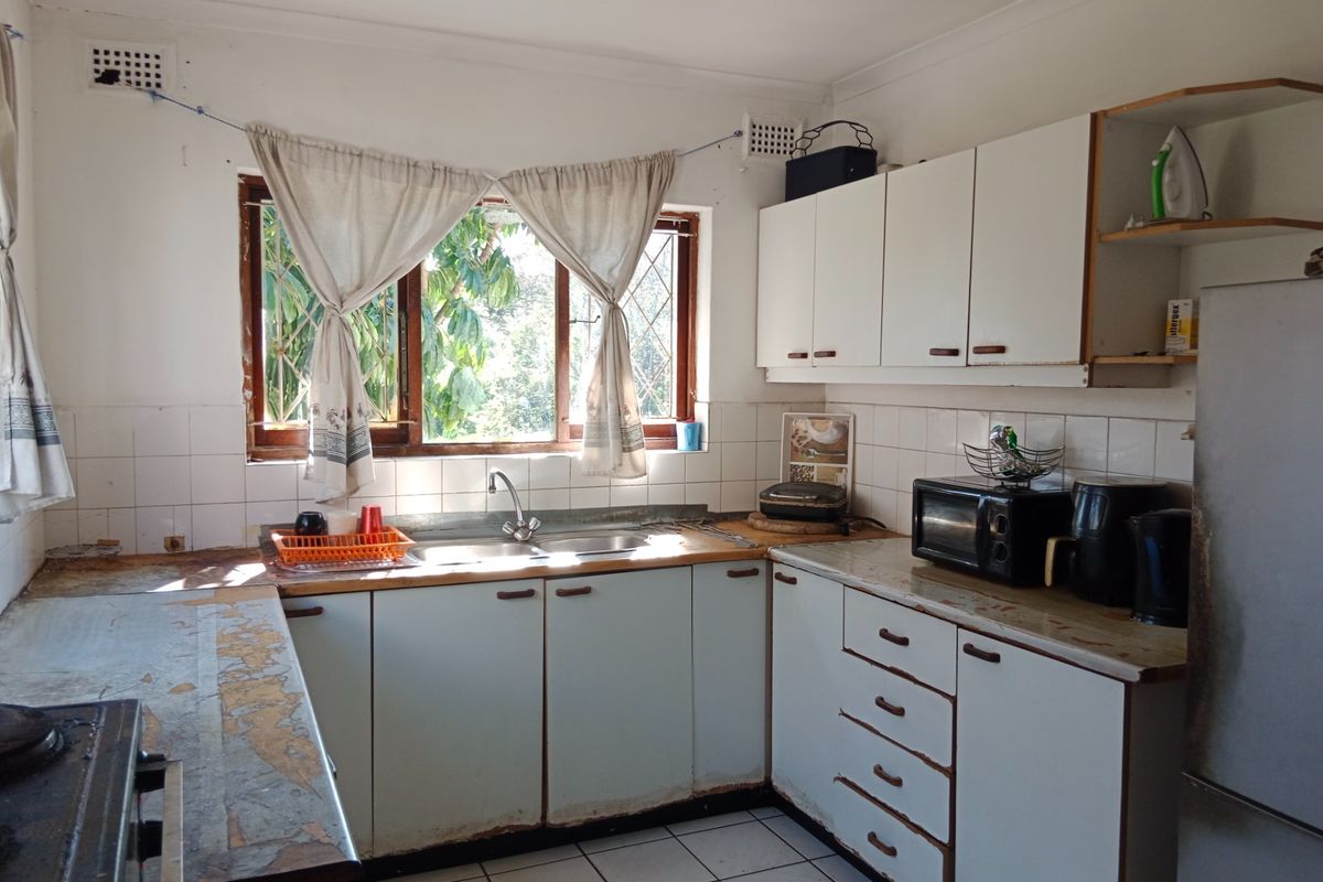 A functional kitchen featuring tiled flooring, a double sink, and ample built-in cabinetry, currently showing signs of wear on countertops and cabinet finishes.