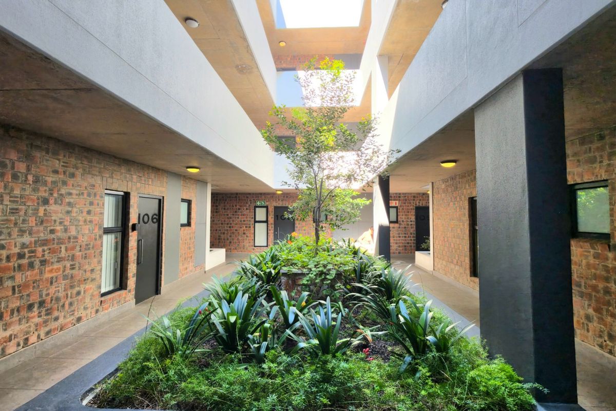 A well-maintained central courtyard featuring exposed brick walls, concrete walkways, and a landscaped garden bed under an open-air atrium.