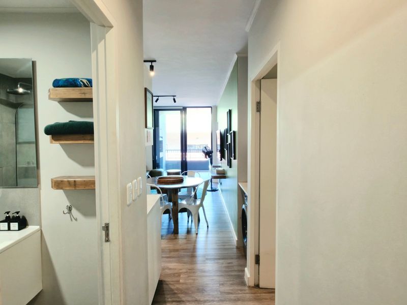 A view through a hallway leading into an open-plan living area with laminate flooring and access to a balcony.