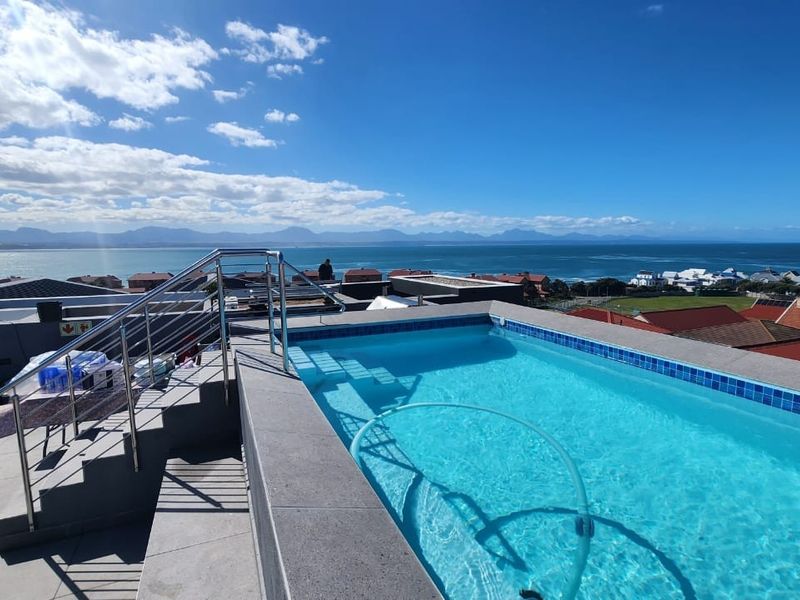 Elevated rooftop swimming pool featuring modern stainless steel railings and panoramic ocean and mountain views.