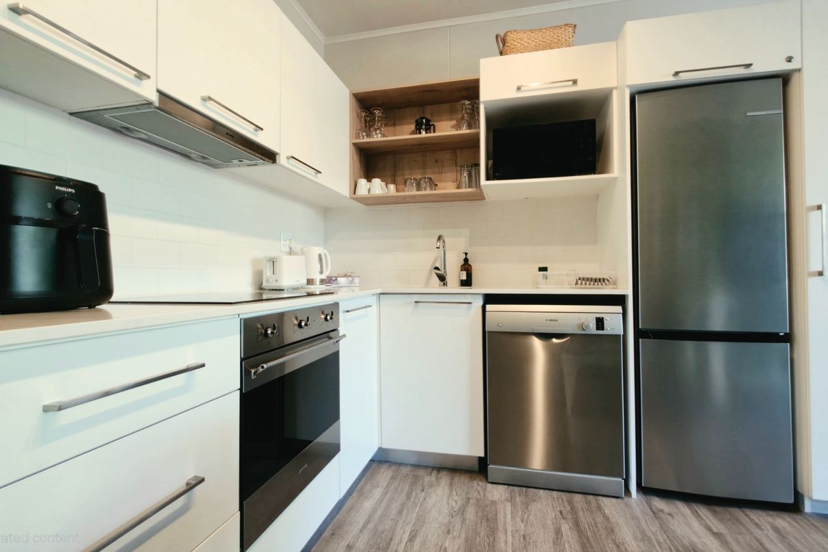 Modern kitchen featuring white cabinetry, subway tile backsplash, integrated stainless steel appliances, and wood-look laminate flooring.