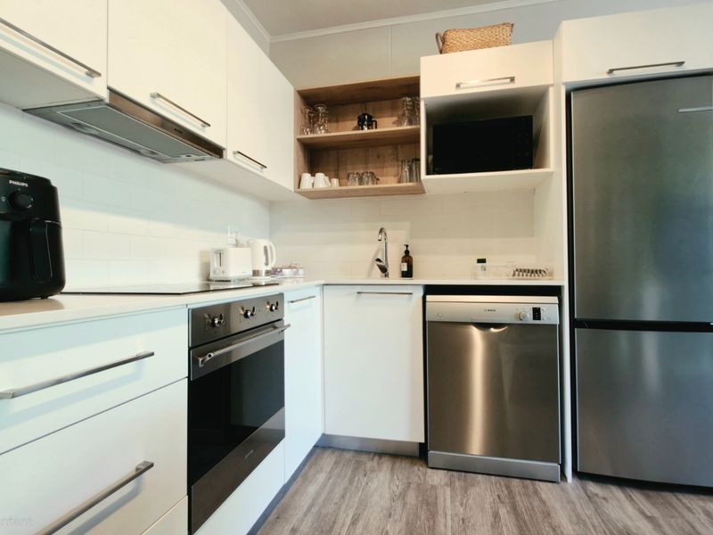 Modern kitchen featuring white cabinetry, subway tile backsplash, integrated stainless steel appliances, and wood-look laminate flooring.