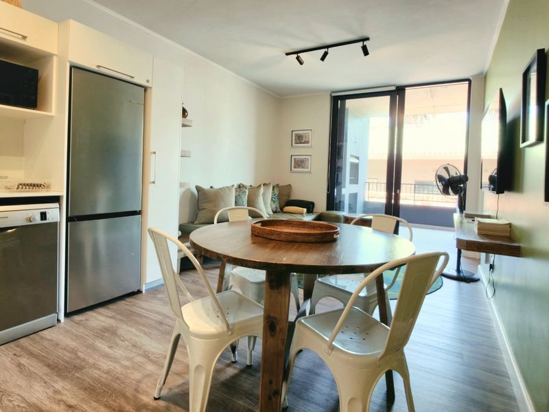 Open-plan living area featuring a modern kitchen with integrated appliances, laminate flooring, and direct access to a private balcony through sliding glass doors.