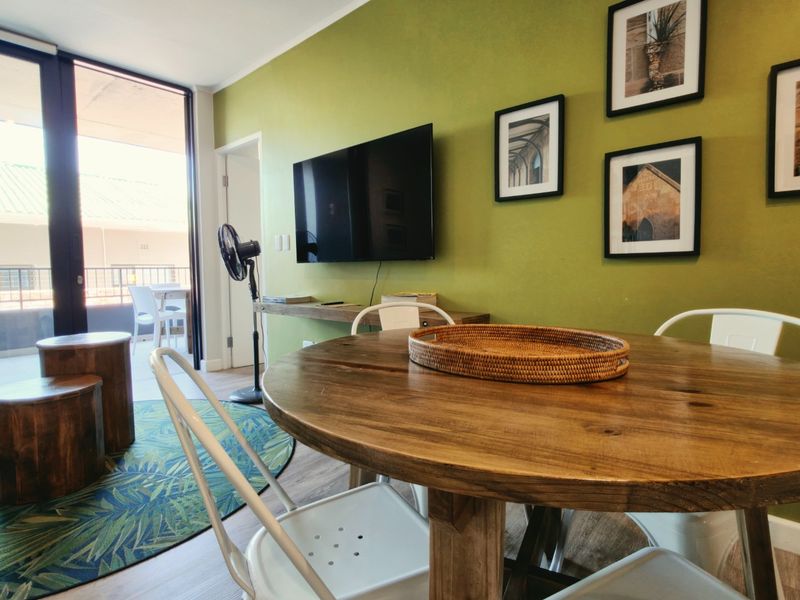 Open plan living area featuring laminate flooring, a wall-mounted television, and large sliding glass doors providing access to an outdoor balcony.