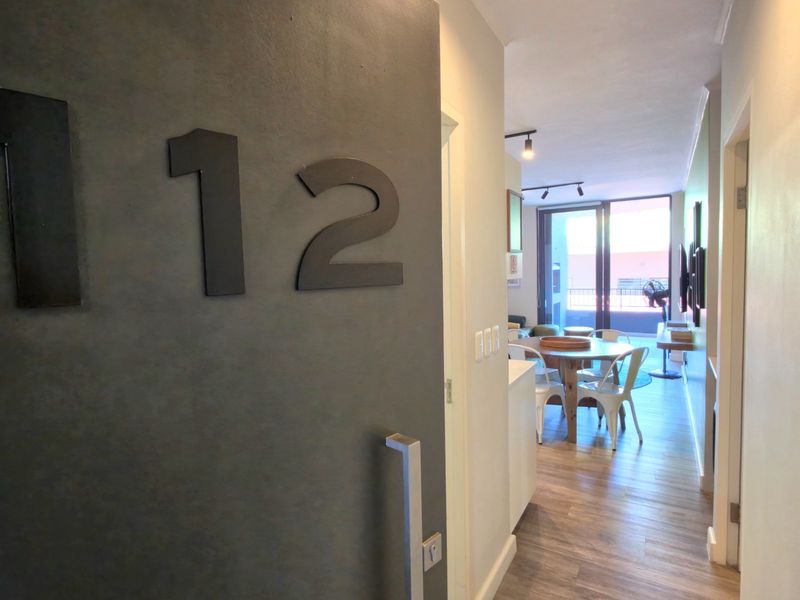 Entrance view into an apartment featuring laminate flooring, modern track lighting, and a direct line of sight to the balcony area.
