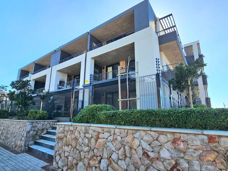 Modern apartment building exterior featuring stone retaining walls, secure electric fencing, and private balconies with concrete finishes.