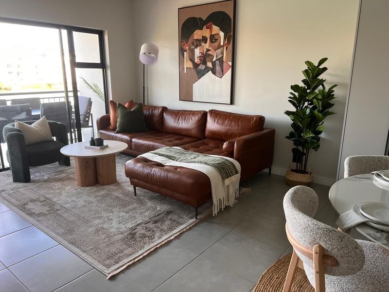 A bright open-plan living area featuring large sliding glass doors that provide access to a balcony and neutral tiled flooring throughout.