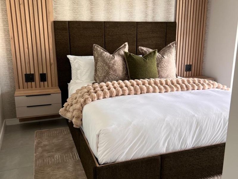 Modern bedroom featuring stylish timber slat wall paneling, integrated floating bedside tables, and neutral tiled flooring.