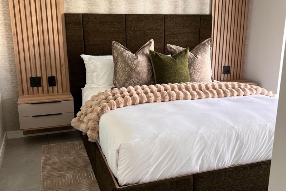 Modern bedroom featuring stylish timber slat wall paneling, integrated floating bedside tables, and neutral tiled flooring.