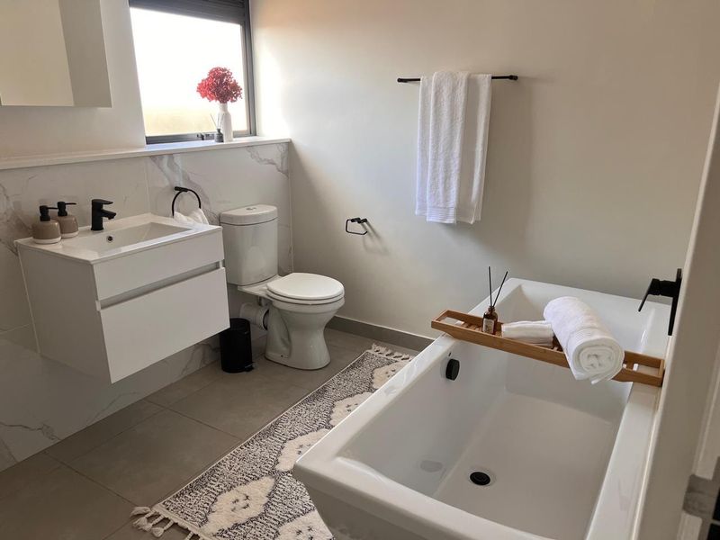Modern bathroom featuring a wall-mounted vanity, freestanding bathtub with black fixtures, and elegant marble-look wall tiling.