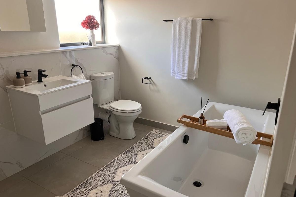 Modern bathroom featuring a wall-mounted vanity, freestanding bathtub with black fixtures, and elegant marble-look wall tiling.