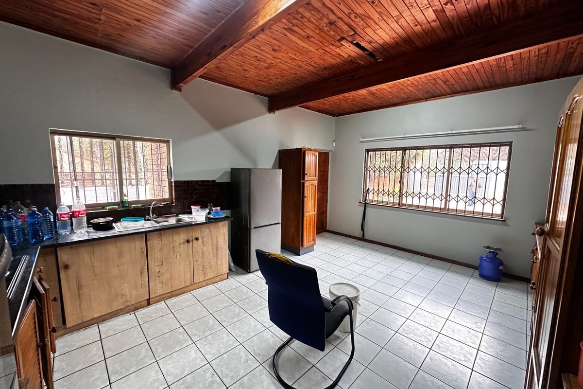 A spacious kitchen featuring timber beam ceilings, tiled flooring, and built-in wooden cabinetry with a stainless steel sink.