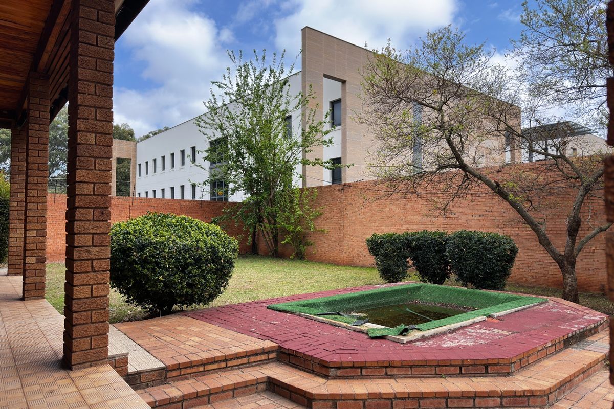 Rear garden area featuring a covered brick veranda, paved patio, and a sunken water feature enclosed by a brick boundary wall.