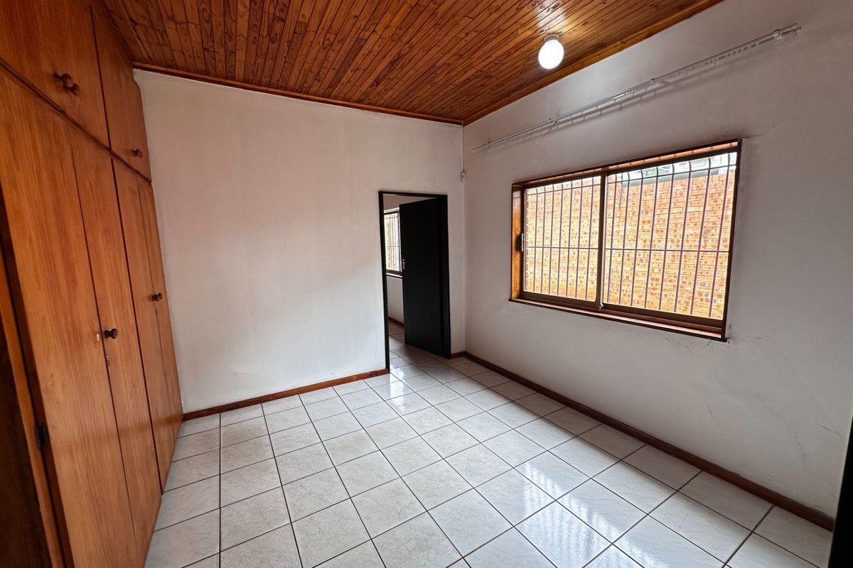 A vacant bedroom featuring tiled flooring, built-in wooden cupboards, and a classic wooden ceiling with security bars on the window.
