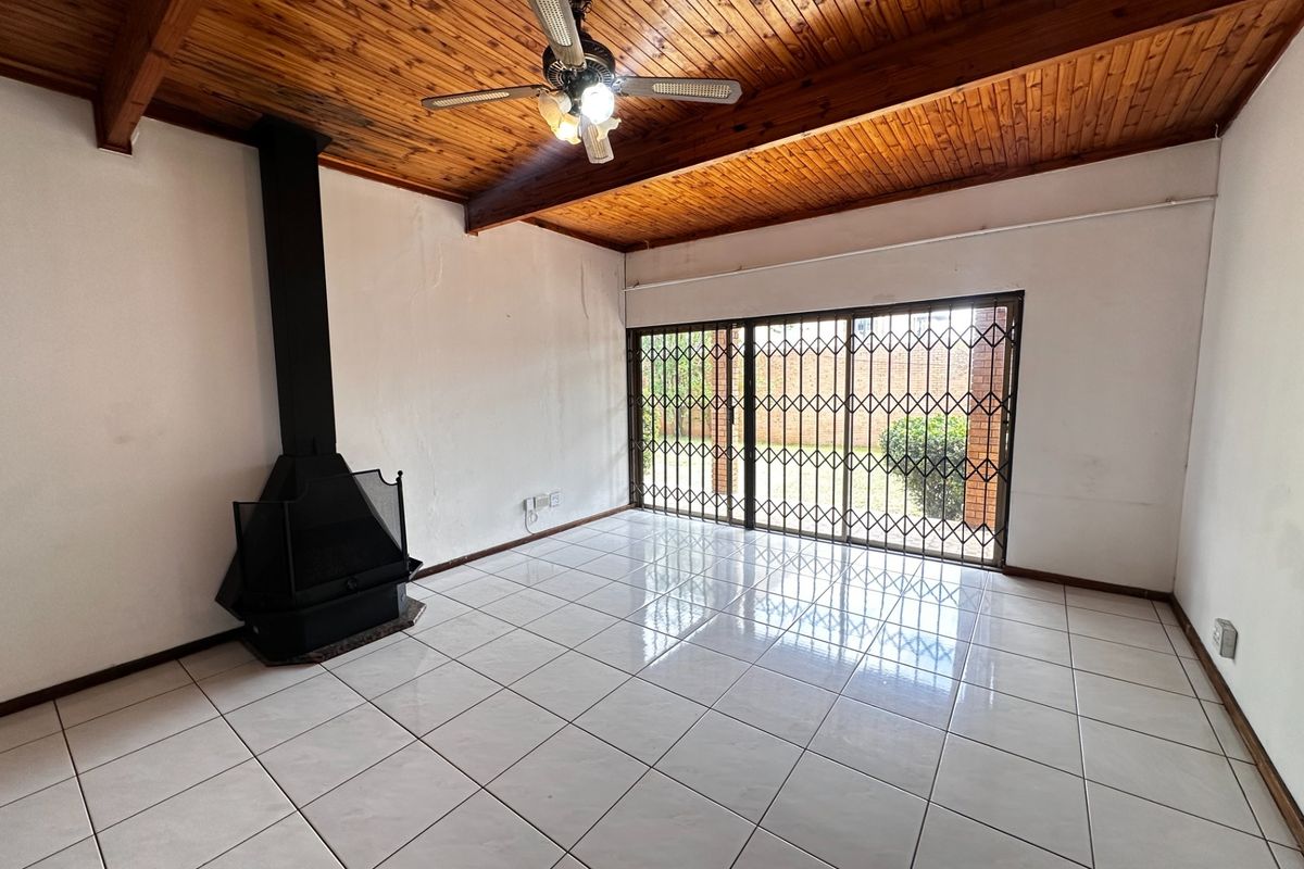 Spacious living room featuring a timber-clad ceiling, tiled flooring, and a freestanding fireplace, with direct access to the garden through sliding glass doors.