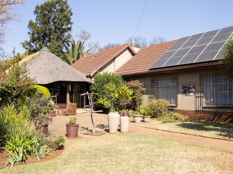 Rear exterior view featuring a paved patio, a traditional thatched lapa, and a main house roof equipped with solar panels.