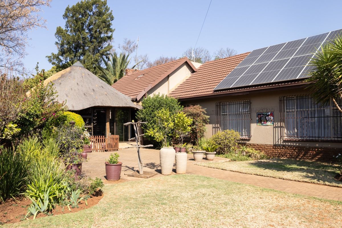 Rear exterior view featuring a paved patio, a traditional thatched lapa, and a main house roof equipped with solar panels.