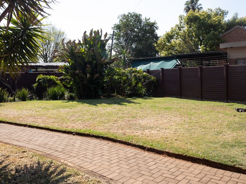 A private rear garden featuring a well-maintained lawn, a paved walkway, and secure perimeter fencing with integrated electric security wires.