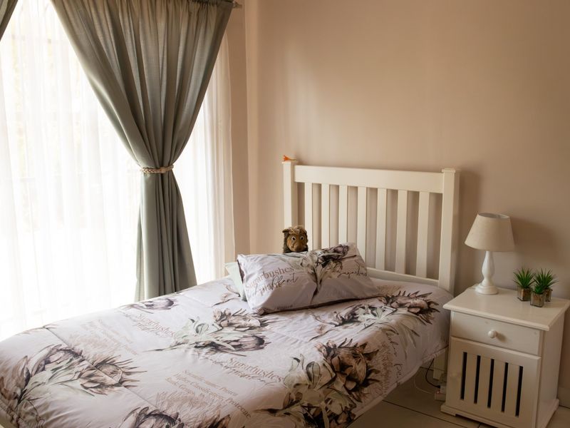 A well-lit bedroom featuring neutral wall tones, tiled flooring, and large windows with installed curtain tracks.