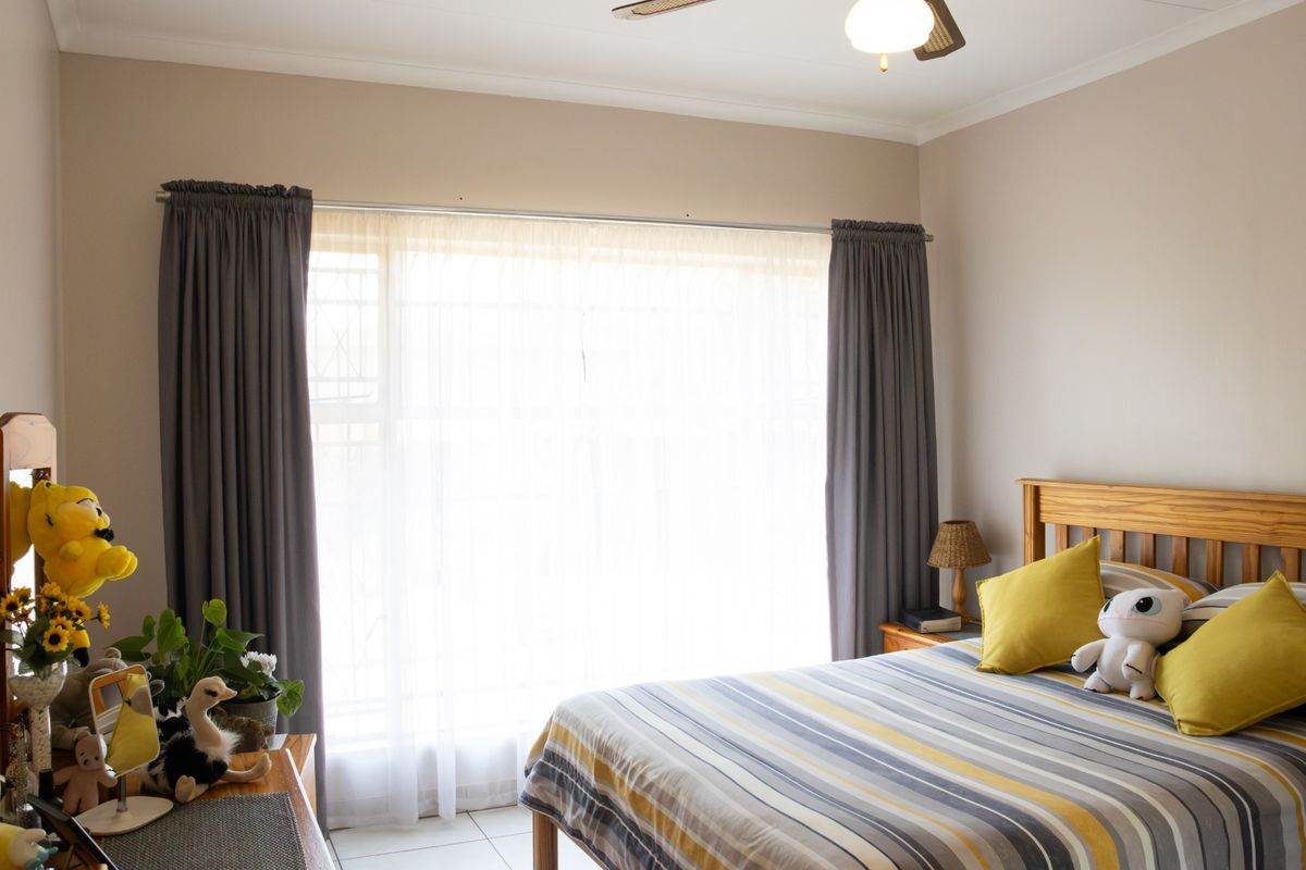 A bedroom featuring tiled flooring, a ceiling fan, and a large window with curtain rod installation.