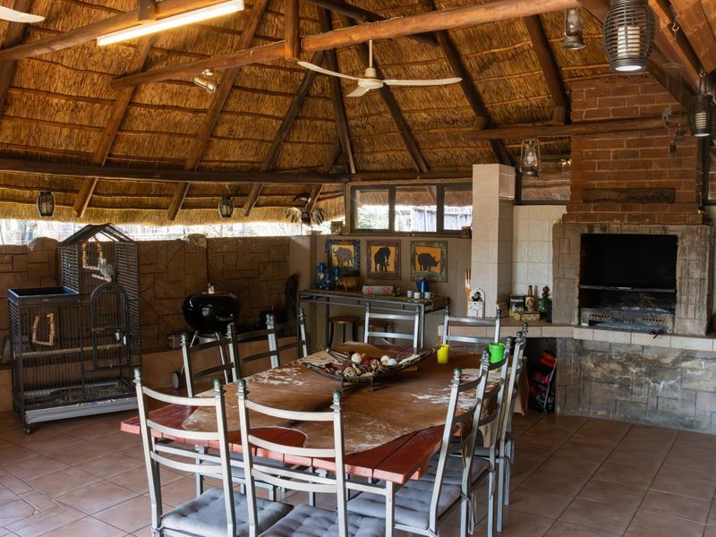 Spacious covered patio featuring a traditional thatched roof, exposed timber rafters, and a built-in brick fireplace, ideal for outdoor entertaining.
