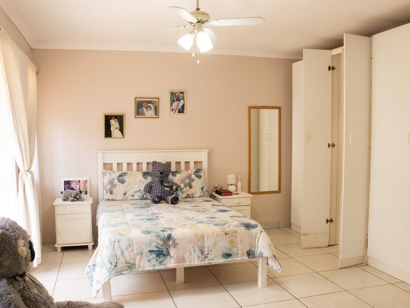 A well-lit bedroom featuring tiled flooring, a ceiling fan, and built-in cupboards for storage.