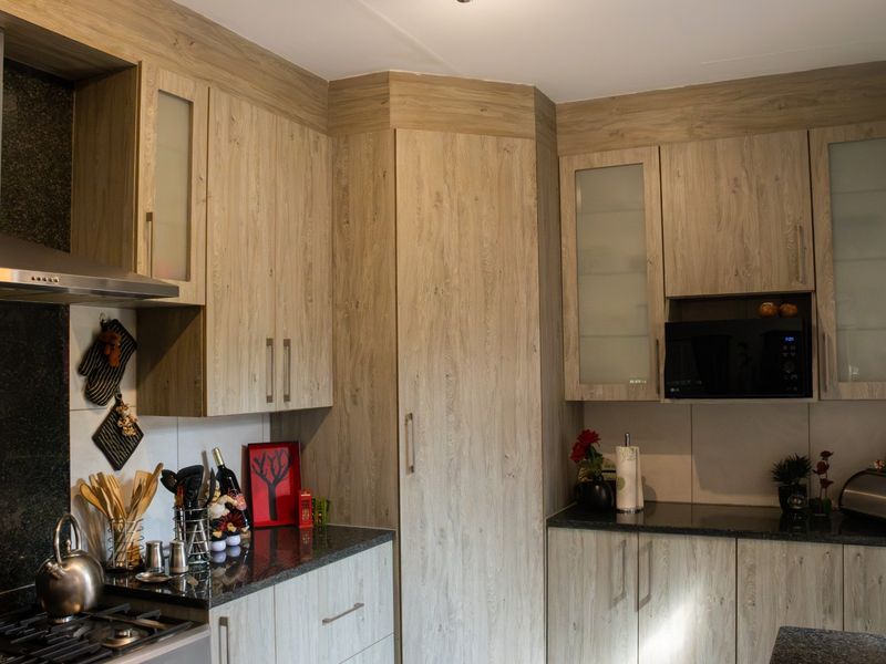 Modern kitchen featuring wood-look cabinetry, granite countertops, a stainless steel extractor fan, and a built-in microwave.