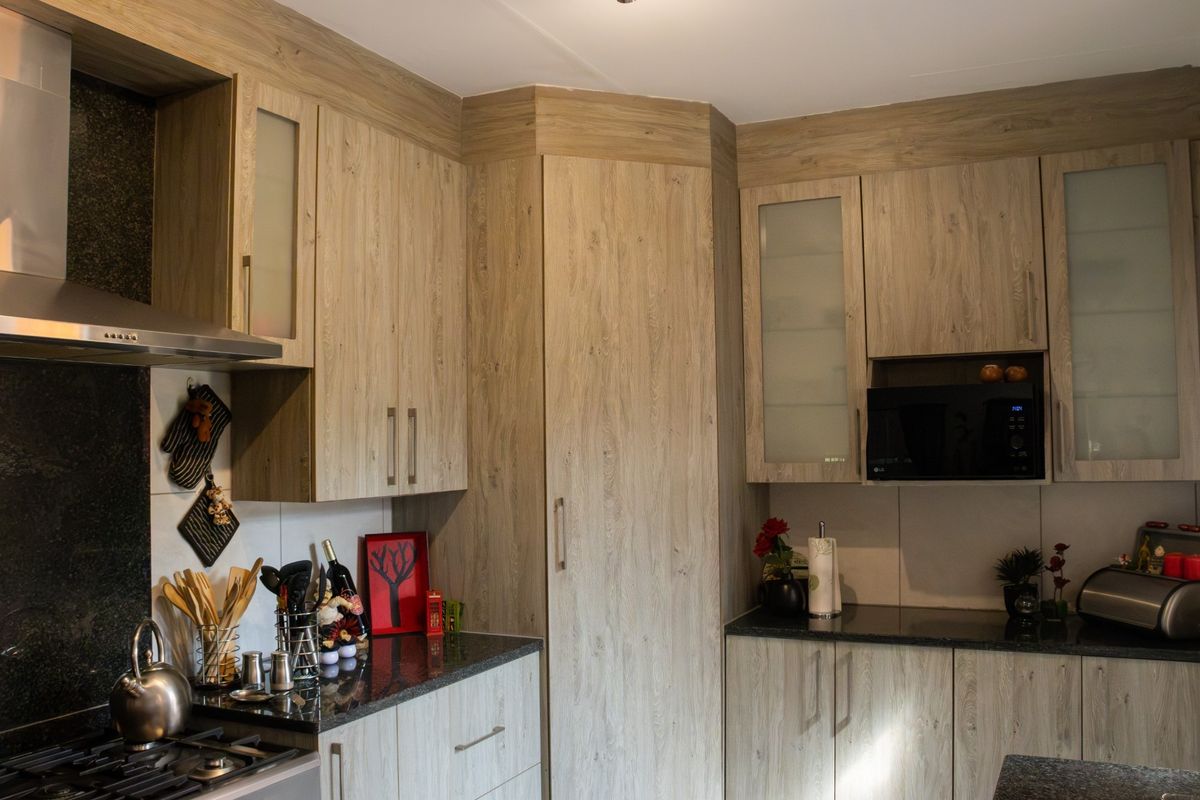 Modern kitchen featuring wood-look cabinetry, granite countertops, a stainless steel extractor fan, and a built-in microwave.