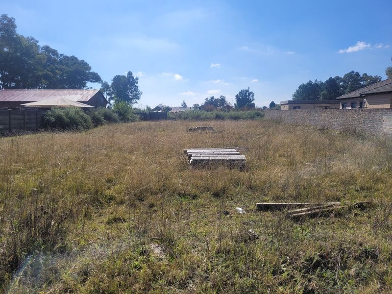 A vacant residential plot featuring overgrown grass and perimeter walling, offering a blank canvas for future development.