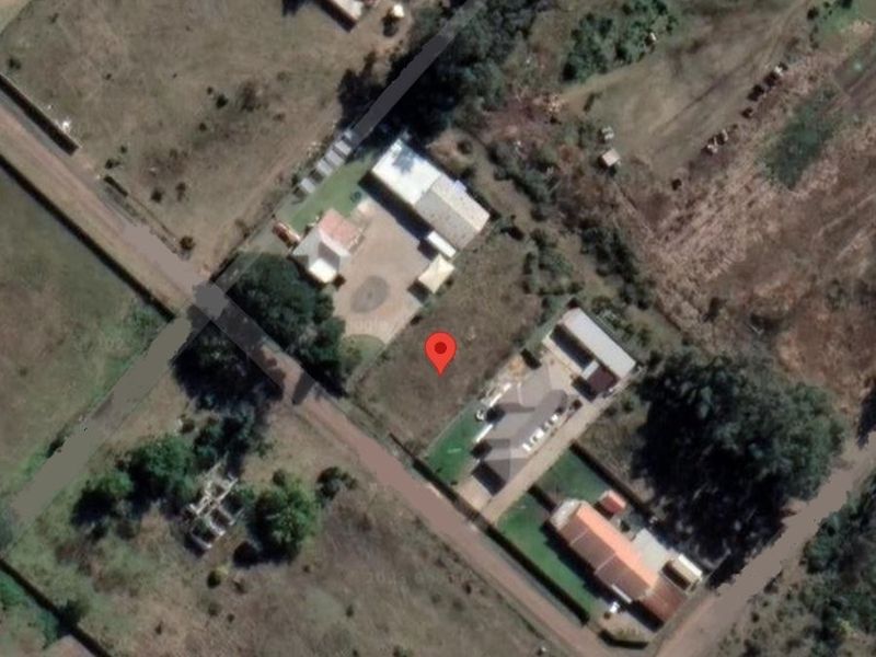 An aerial view of a vacant residential plot situated within a developed neighborhood, showing surrounding properties and access roads.