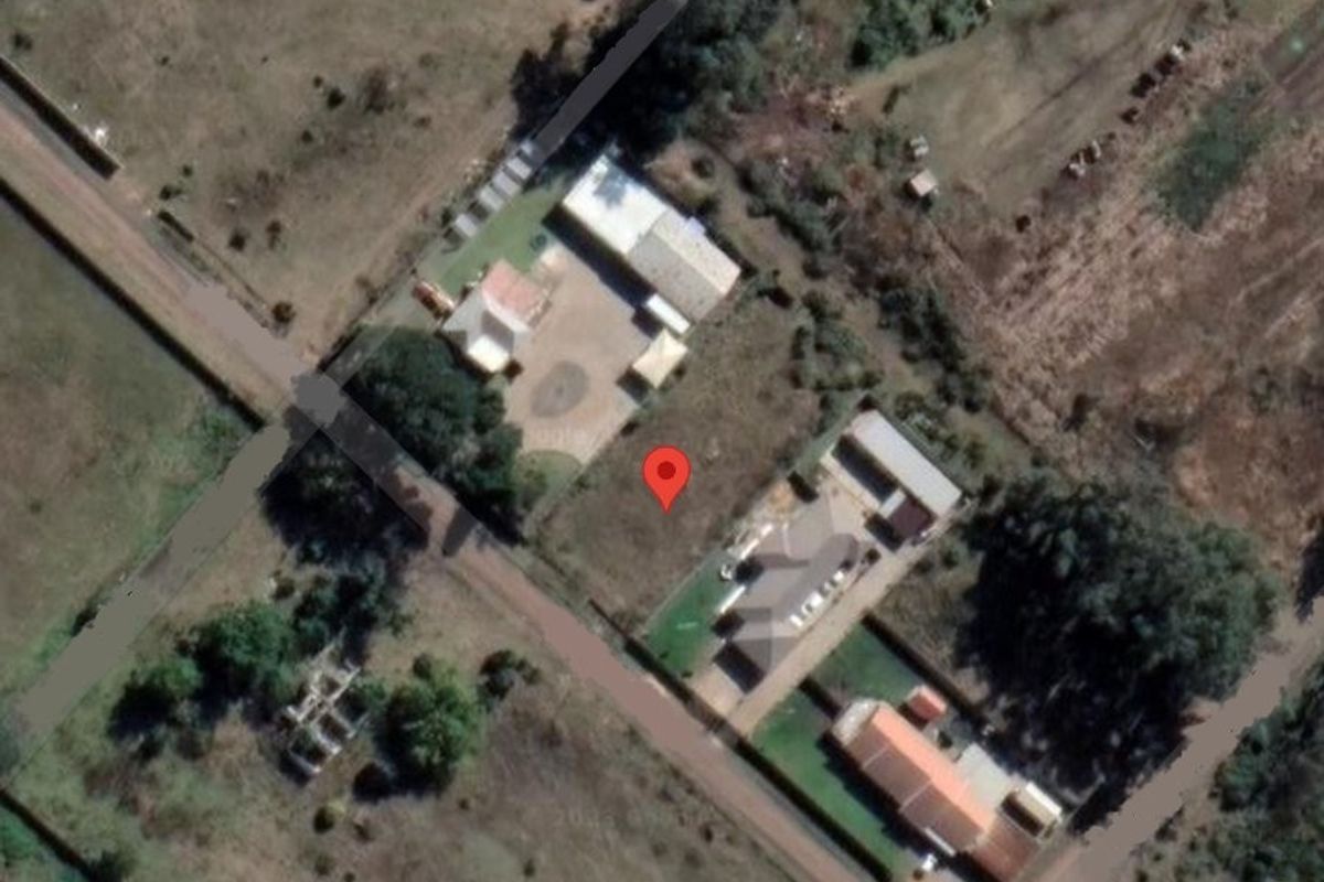 An aerial view of a vacant residential plot situated within a developed neighborhood, showing surrounding properties and access roads.