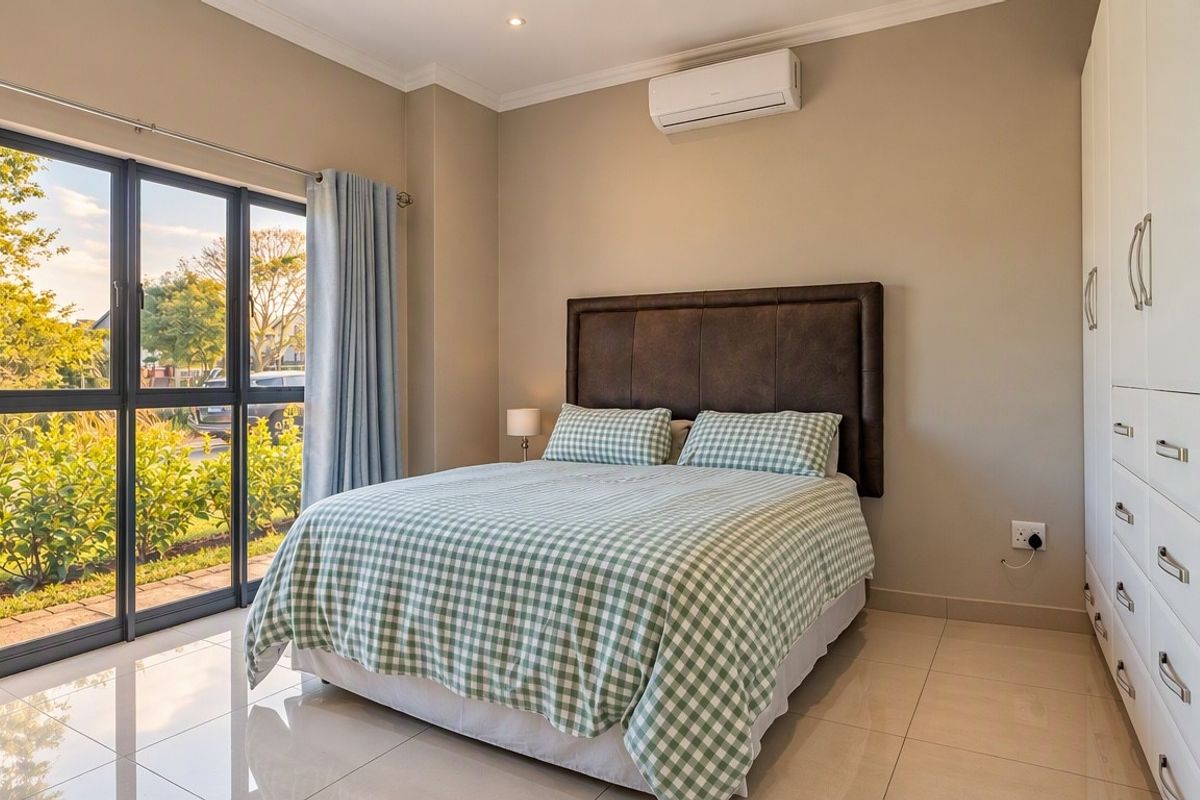 A well-maintained bedroom featuring tiled floors, built-in cupboards, a split-system air conditioner, and a large sliding glass door providing natural light and garden access.