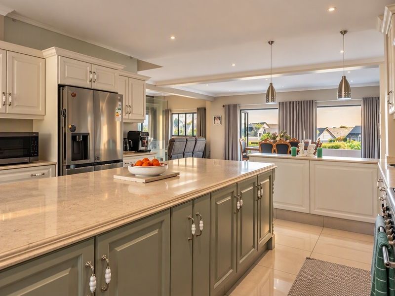 Spacious open-plan kitchen featuring a large central island, stone countertops, shaker-style cabinetry, and high-end integrated appliances, flowing seamlessly into the dining and living areas.