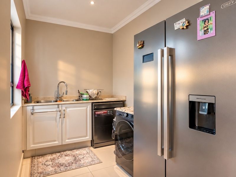 A functional laundry room featuring built-in cabinetry, a stainless steel sink, and tiled flooring, providing a clean and organized utility space.