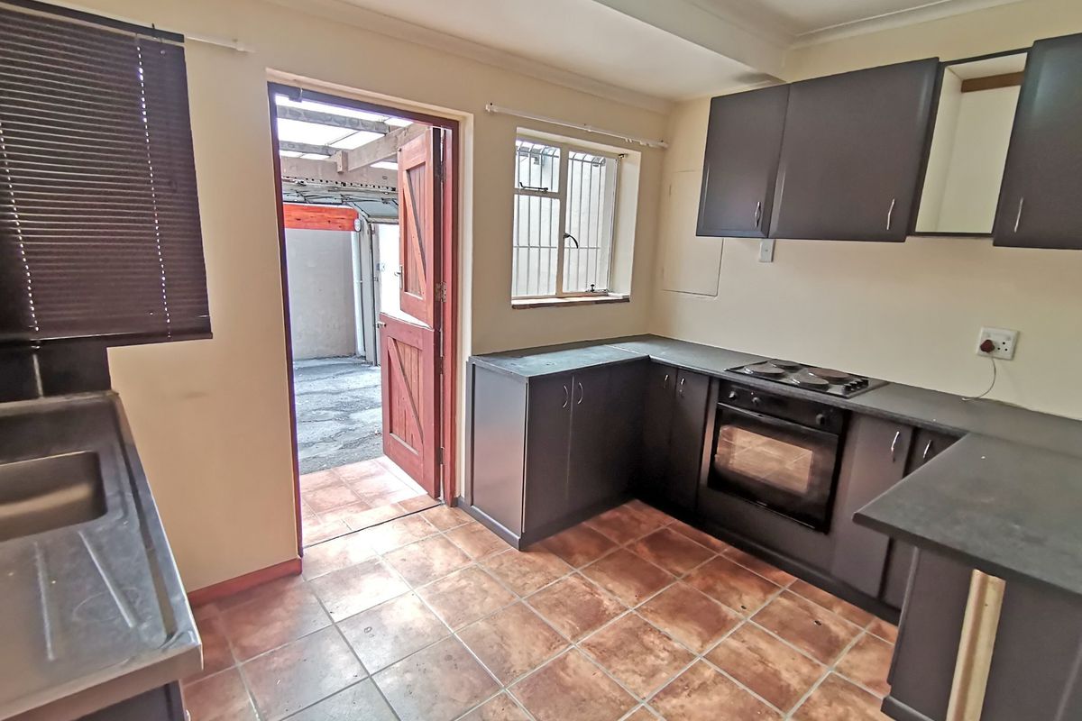 A functional kitchen featuring dark cabinetry, built-in oven and hob, tiled flooring, and direct access to an outdoor area.